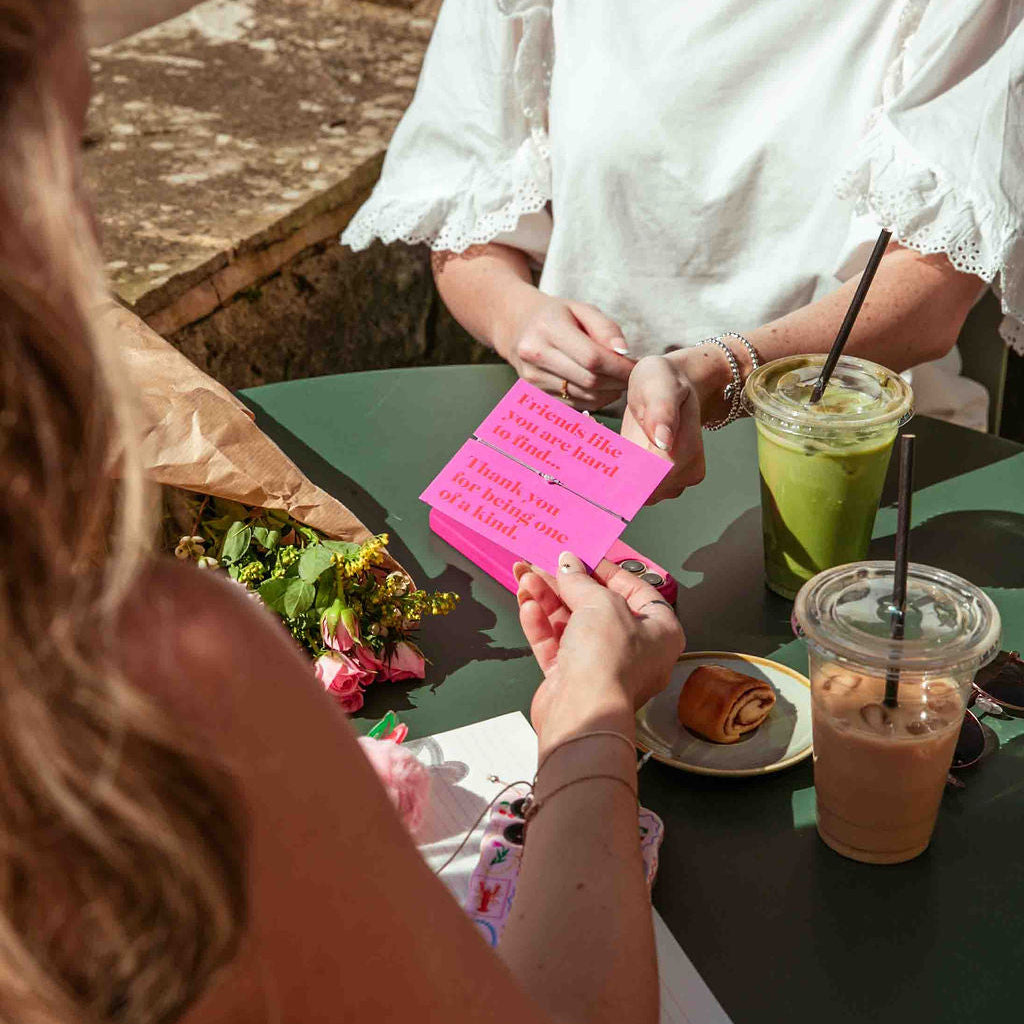 Two people sitting at a table outdoors with drinks and food.