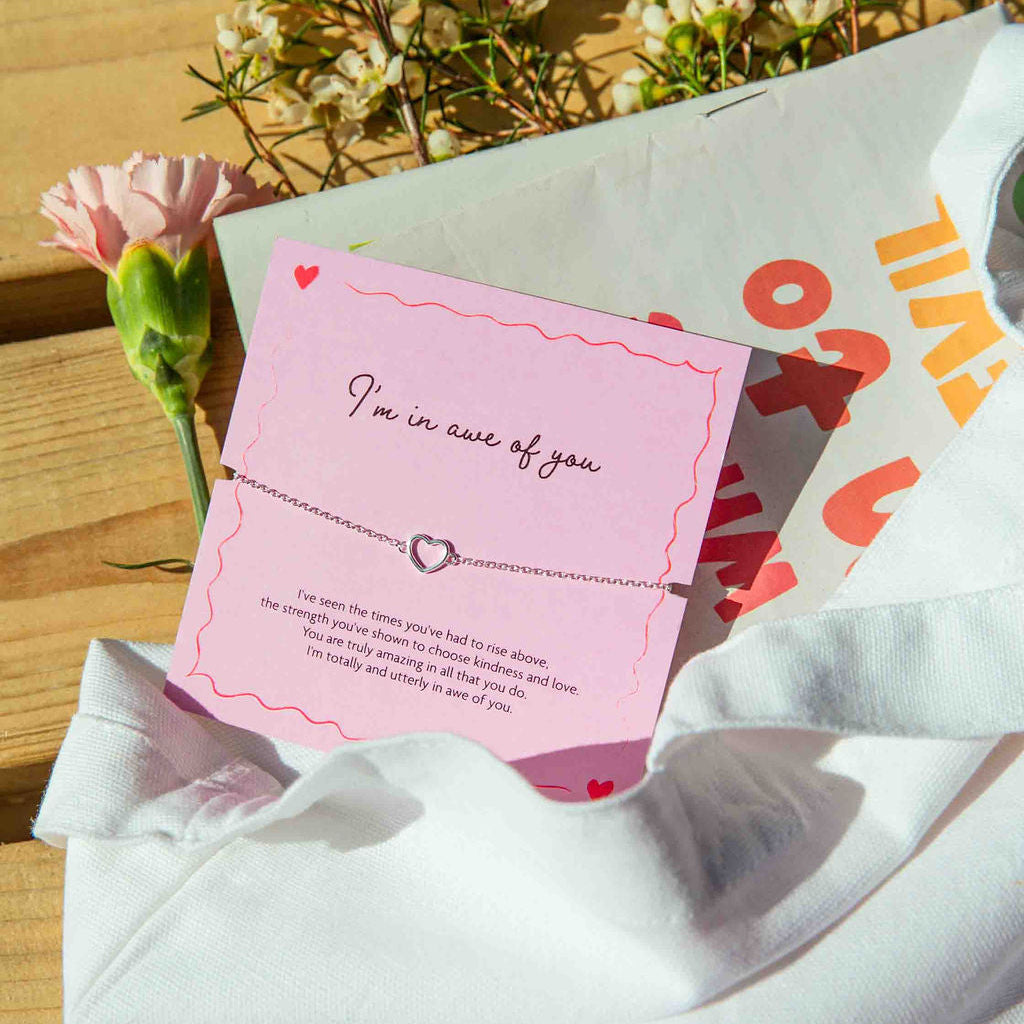Card with 'I'm in awe of you' message and heart charm on a pink card with red text, surrounded by flowers on a wooden surface.