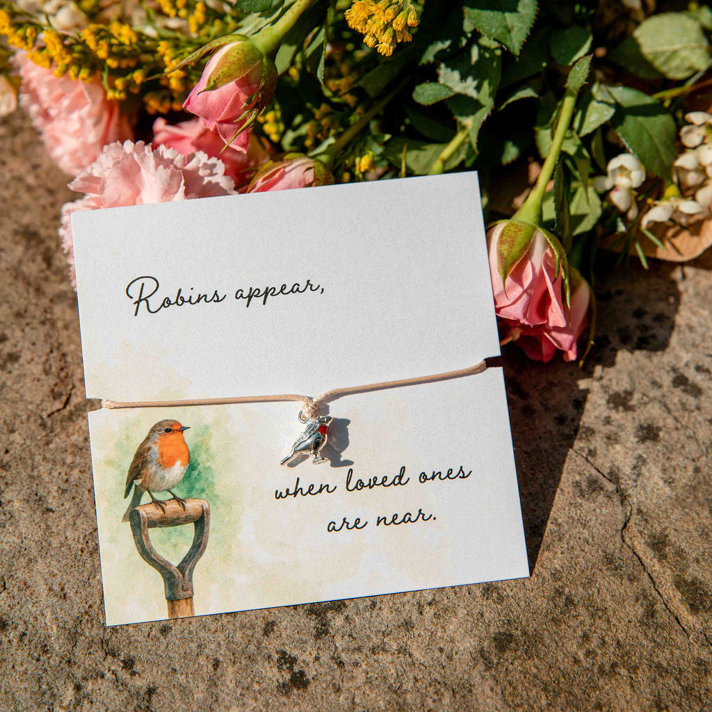 Bouquet of flowers with a card featuring a robin illustration and text on a stone surface.