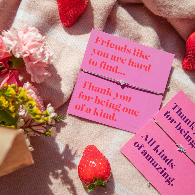 Pink cards with heartfelt messages surrounded by flowers and strawberries on a soft surface