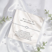 Card with 'Will you be my bridesmaid?' question on a white satin background with silver hollow heart bracelet. A perfect gift for bridesmaid proposal boxes.
