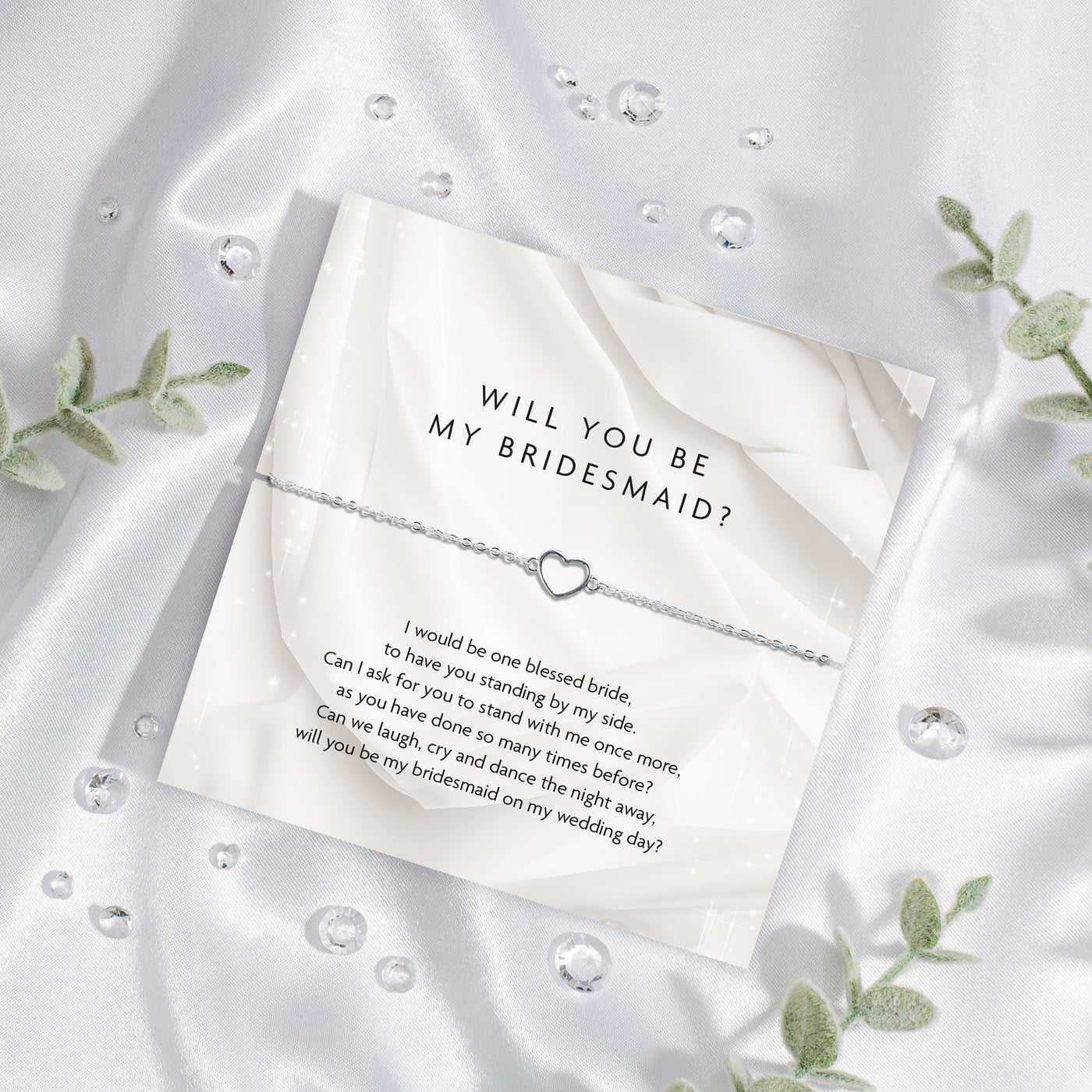Card with 'Will you be my bridesmaid?' question on a white satin background with silver hollow heart bracelet. A perfect gift for bridesmaid proposal boxes.