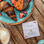 Dessert plate with pastries and berries on a wooden table, next to a coffee cup and a Brunch Club Bracelet and card.