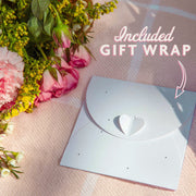Gift wrap with heart design on a pink blanket with flowers, the text reads 'included gift wrap' with an arrow pointing to the envelope