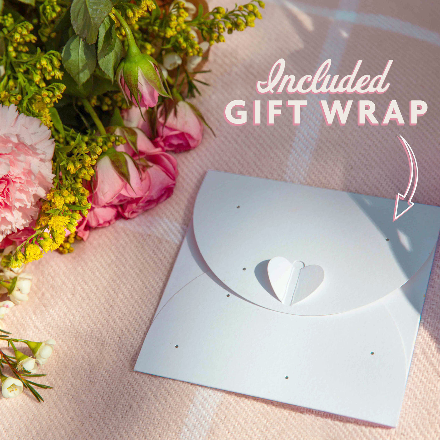 Gift wrap with heart design on a pink blanket with flowers, the text reads 'included gift wrap' with an arrow pointing to the envelope
