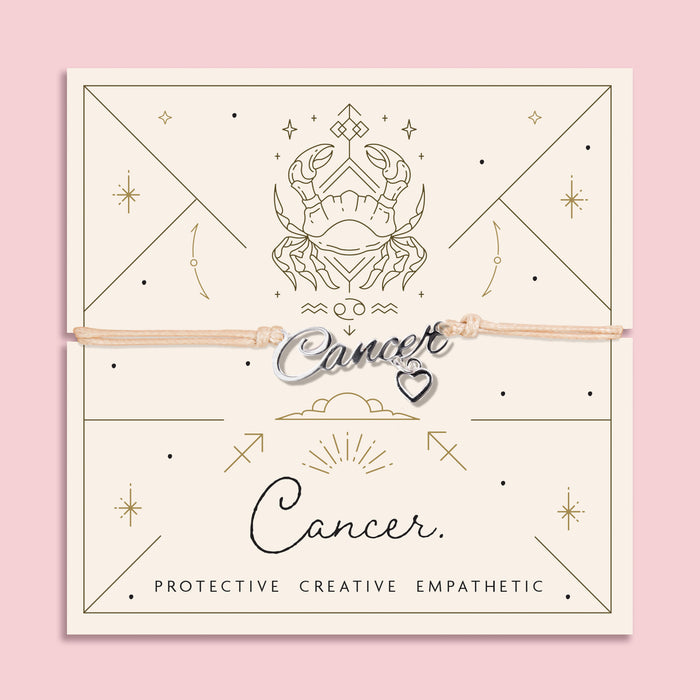 Adjustable beige cord bracelet with a silver 'Cancer' charm and small heart pendant, displayed on a zodiac-themed card featuring a crab illustration and the traits "Protective, Creative, Empathetic".
