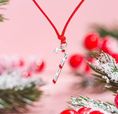 A close-up image of a candy cane bracelet charm with festive decorations in the background.