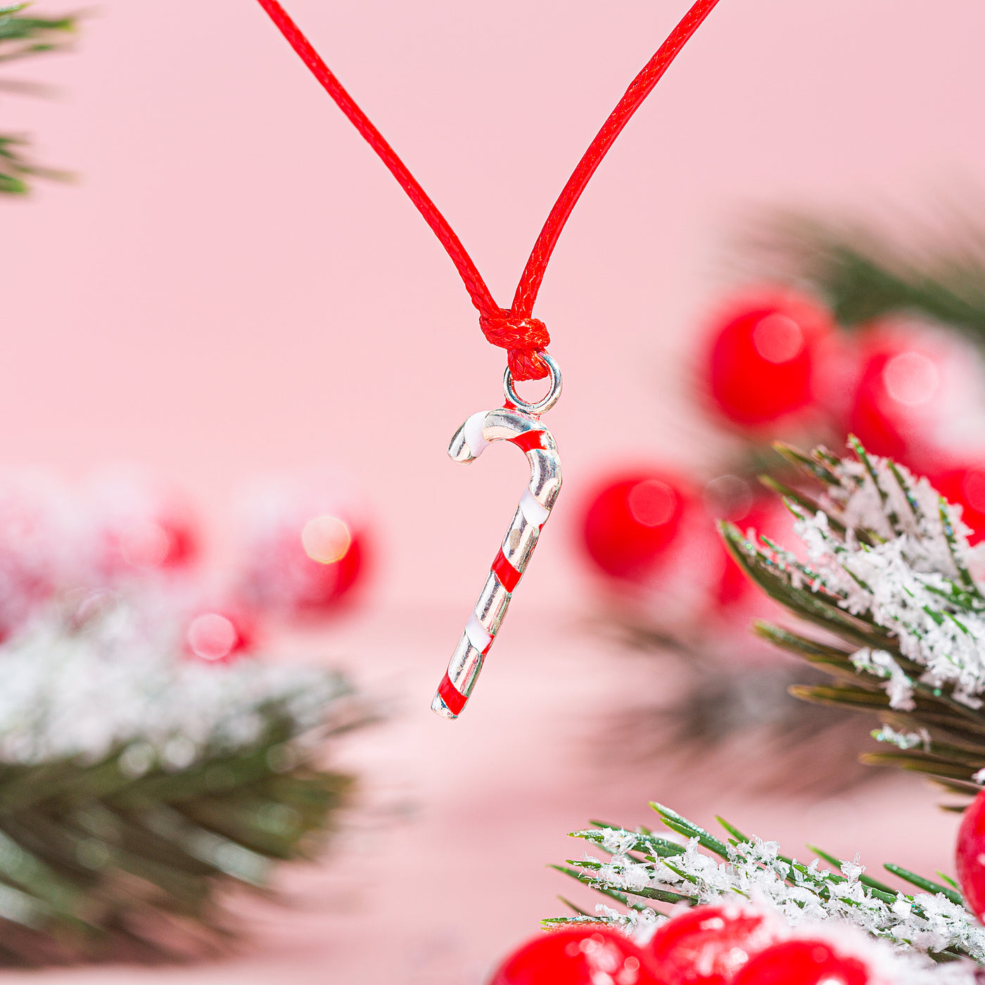 A close-up image of a candy cane bracelet charm with festive decorations in the background.
