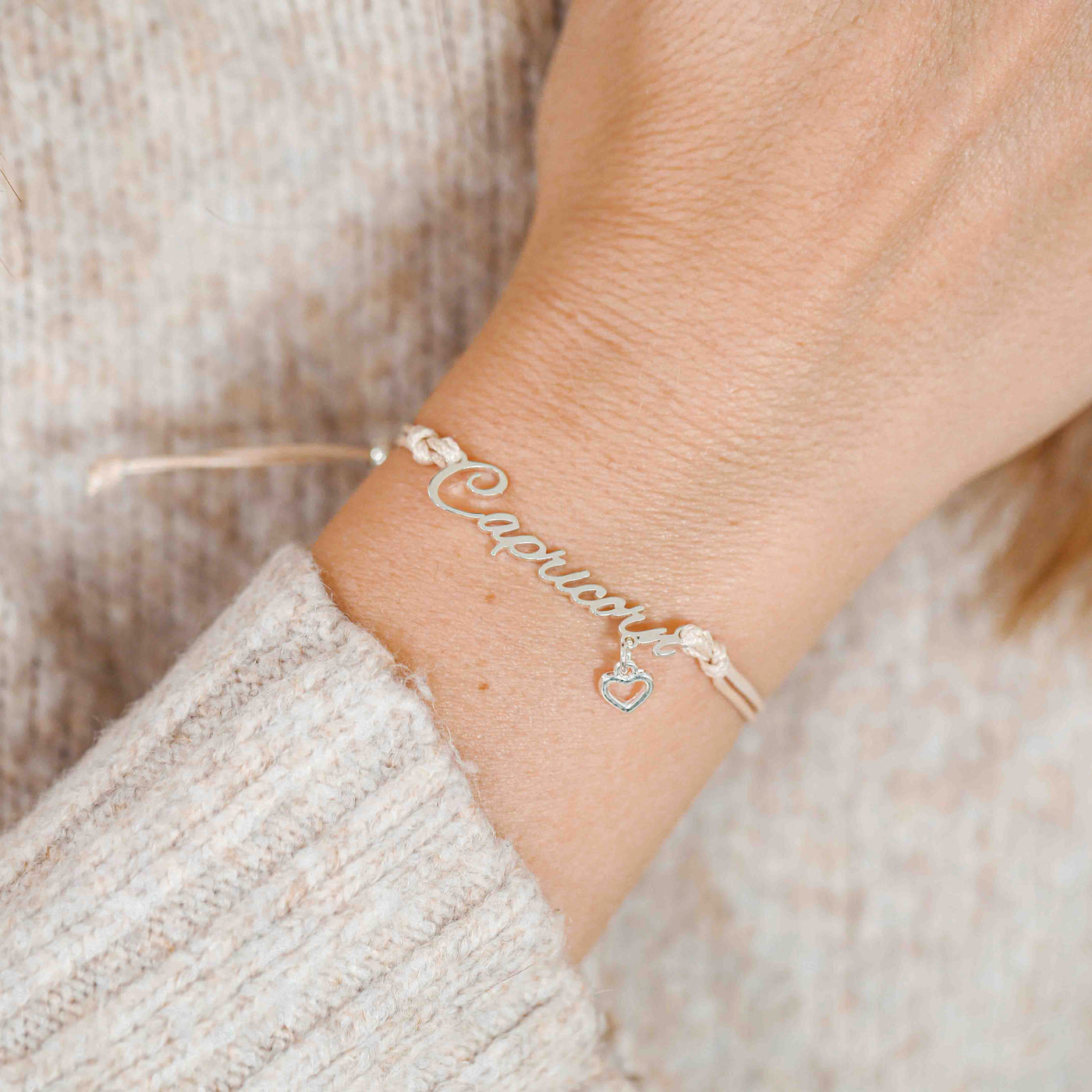 A woman wearing a dainty bracelet with the word “Capricorn” and a tiny heart charm, a meaningful zodiac-inspired gift for her.