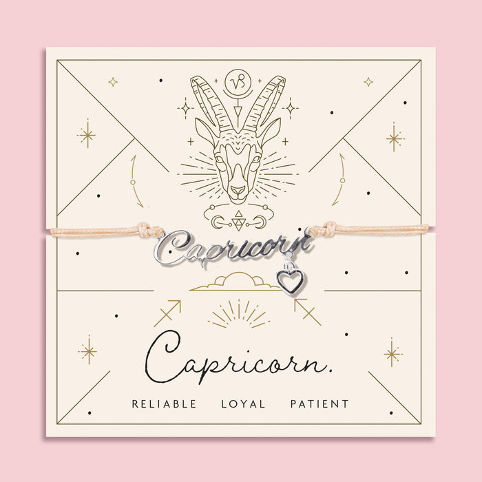 Adjustable peach cord bracelet with a silver 'Capricorn' charm and heart pendant, displayed on a zodiac-themed card featuring a goat illustration and traits reading "Reliable, Loyal, Patient".