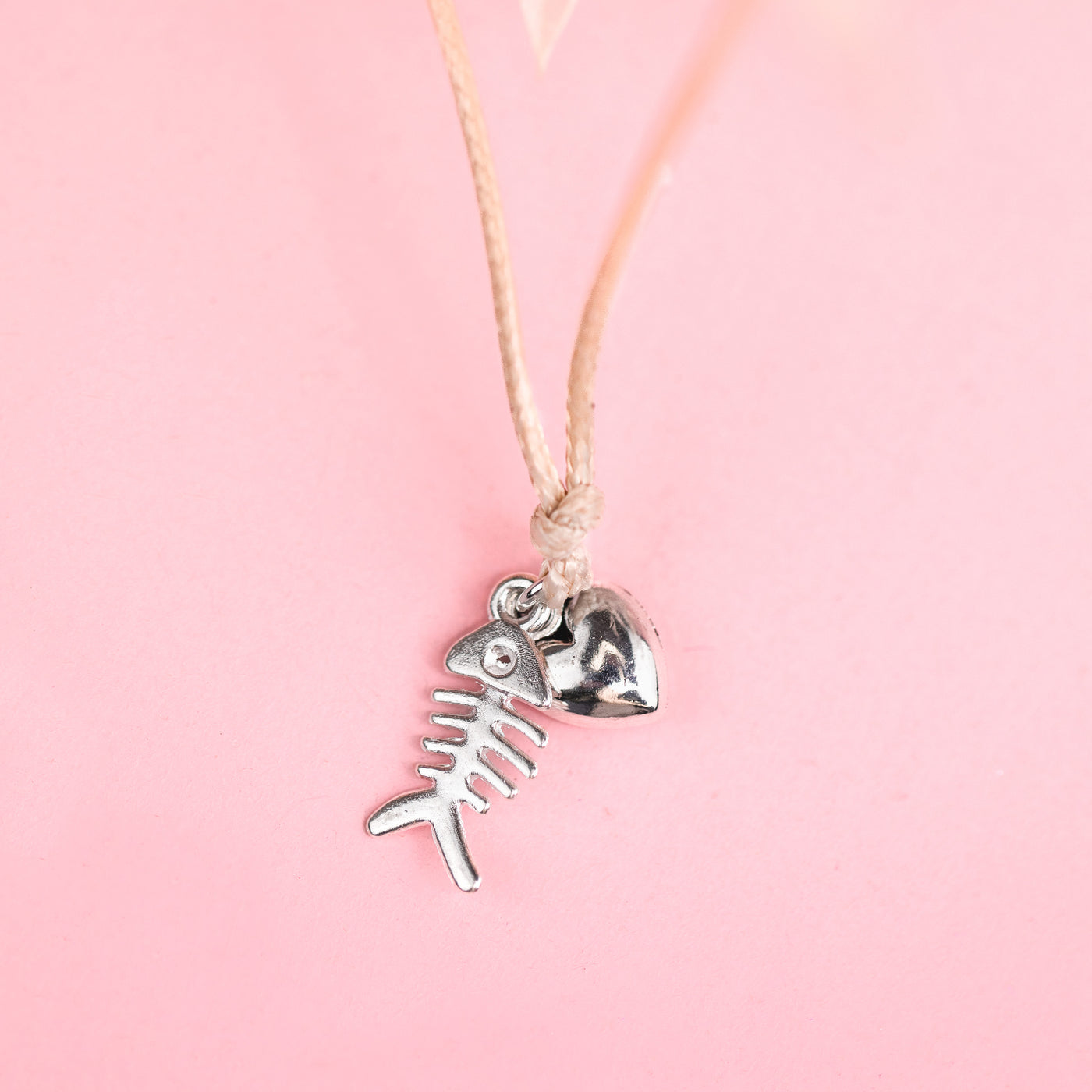 Christmas bracelet with silver fish and heart charm. A cute gift for a cat mum for Xmas. Set on a pink background.