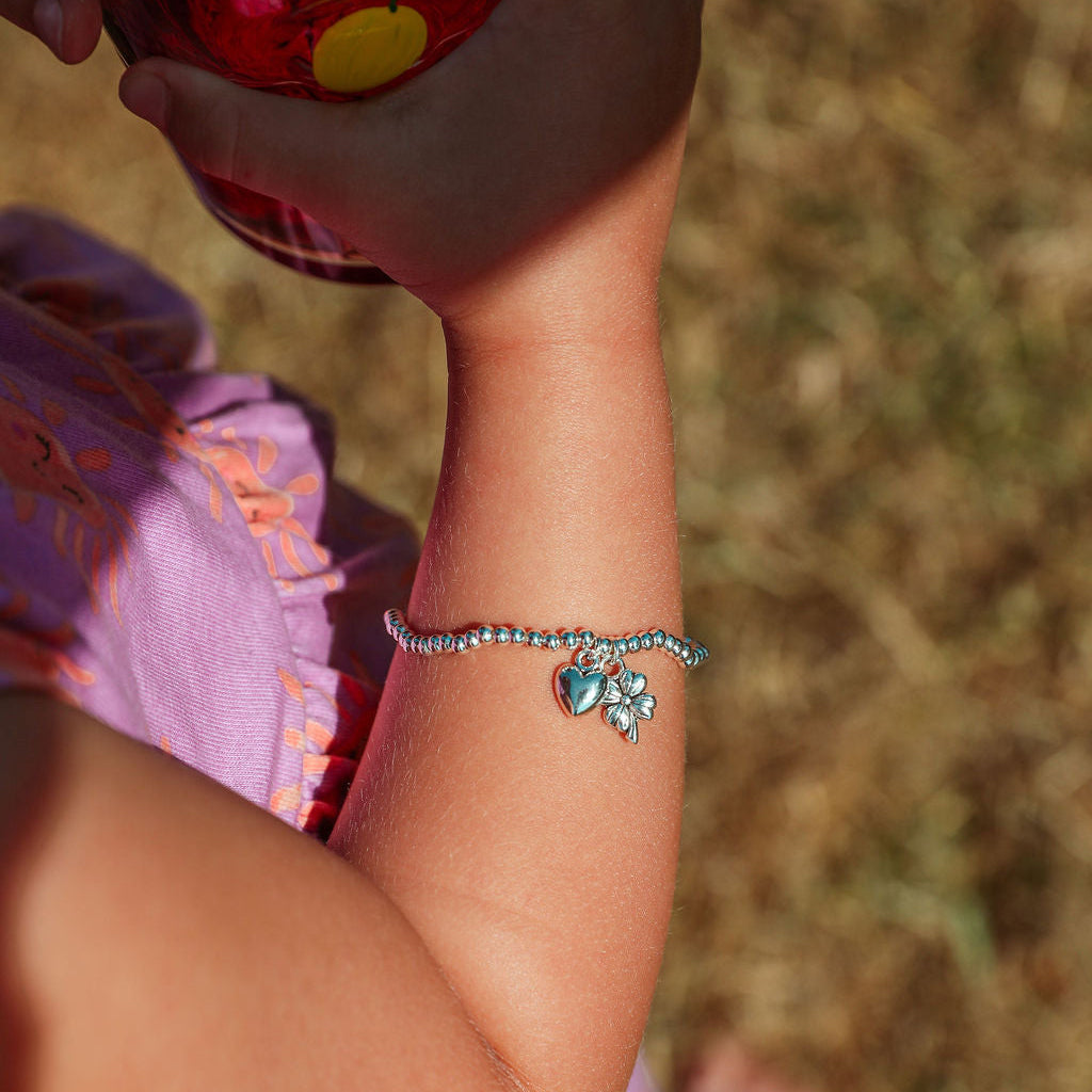 A close-up of a child's arm wearing a silver beaded bracelet with a clover good luck charm, while holding a red cup outdoors.
