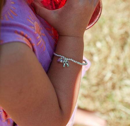 A close-up lifestyle shot of a child wearing a delicate silver beaded bracelet with a small butterfly charm, holding a red cup outdoors.