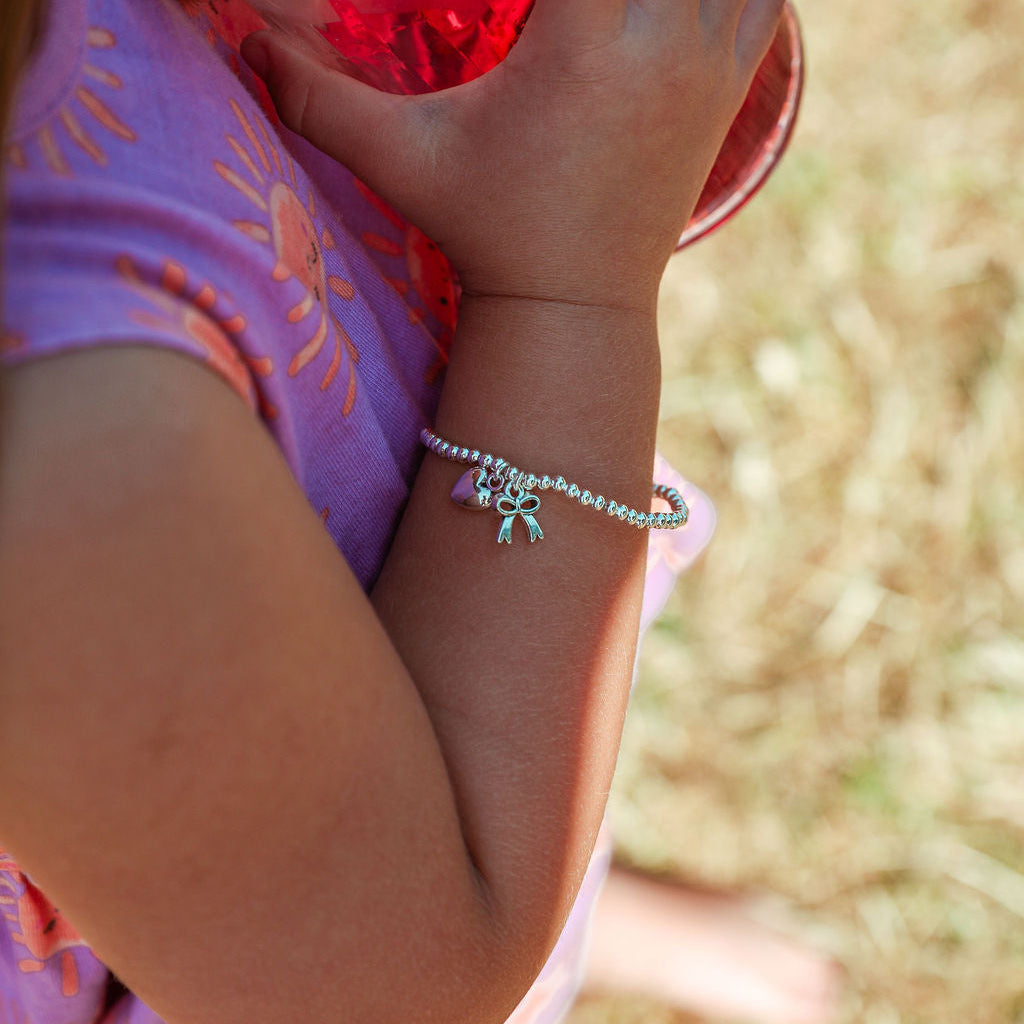 A close-up lifestyle shot of a child wearing a delicate silver beaded bracelet with a small butterfly charm, holding a red cup outdoors.
