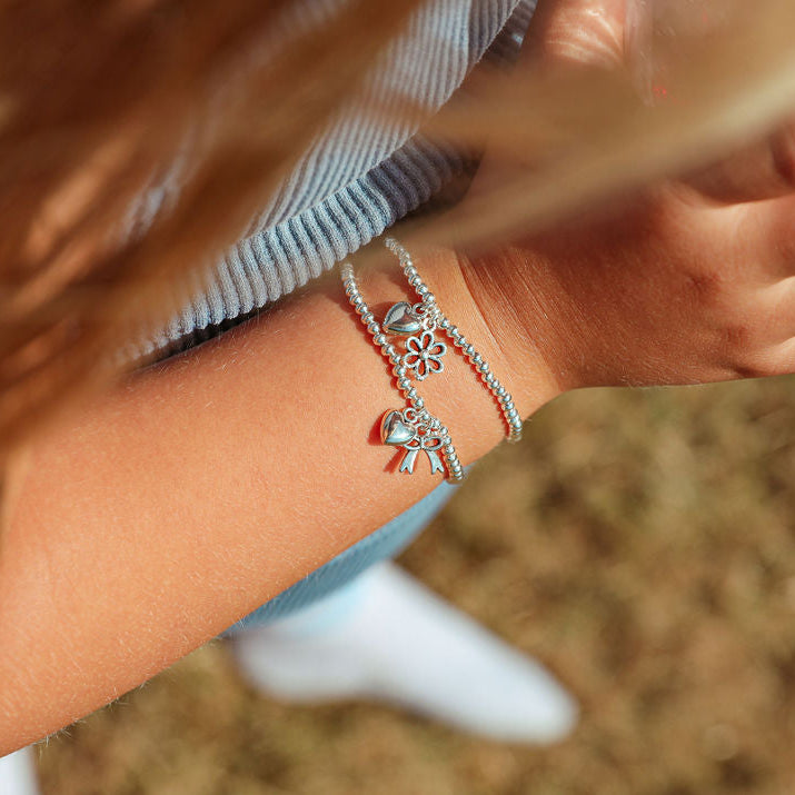 a child wearing two silver beaded bracelets with adorable charms. Set in a field the child is wearing a blue top.