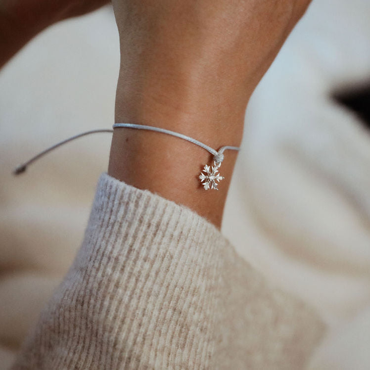 Close-up of a wrist wearing a delicate bracelet with a snowflake charm, against a neutral background.