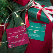 Two wrapped Christmas gift boxes with red and white ribbons and matching gifts from Letterbox Love are arranged on a dark green fabric surface with fairy lights and evergreen branches. The bracelets are elegant gifts for a friend at Christmas.