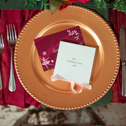 A styled holiday table setting featuring a large gold charger plate, deep burgundy napkins, silver cutlery, and a small white gift box tied with a white ribbon that reads 'Letterbox Love'.