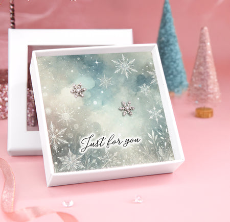 A pair of silver star earrings displayed on a card with a beautiful winter village scene, featuring the text 