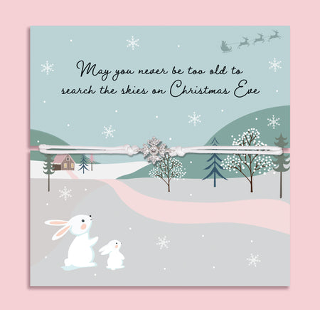 Christmas Eve bracelet featuring a sparkling cubic zirconia snowflake charm on an adjustable cord, presented on a festive card with snowy hills, winter trees, rabbits, and the message “May you never be too old to search the skies on Christmas Eve.” Includes a soft white pouch for gifting and safekeeping. A thoughtful Christmas Eve surprise, festive jewellery gift, or stocking filler for loved ones of all ages, symbolising the magic and sparkle of the holiday season.