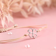 A close-up of a friendship bracelet with beige cord and silver-plated clover bracelet charm. A good luck gift for a friend under £10