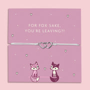 A lilac adjustable bracelet featuring two interlinked heart charms, displayed on a lilac backing card with the playful message "For Fox Sake, You’re Leaving?!" accompanied by cute fox illustrations. Perfect as a farewell gift.