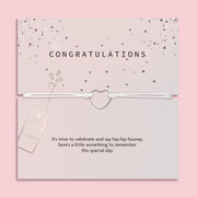 Letterbox Love 'Congratulations' bracelet – delicate silver heart charm on a white cord, presented on a pink confetti card with a champagne bottle design and celebratory message. A thoughtful letterbox gift for graduation, new job, engagement or promotion. Affordable jewellery gift to mark a special milestone for her.