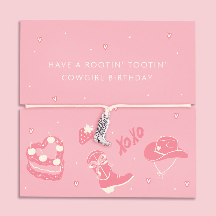 A pink adjustable bracelet featuring a silver-plated cowboy boot charm, displayed on a playful pink backing card with the message "Have a Rootin' Tootin' Cowgirl Birthday" and cowgirl-themed illustrations, including a hat, boots, and cake