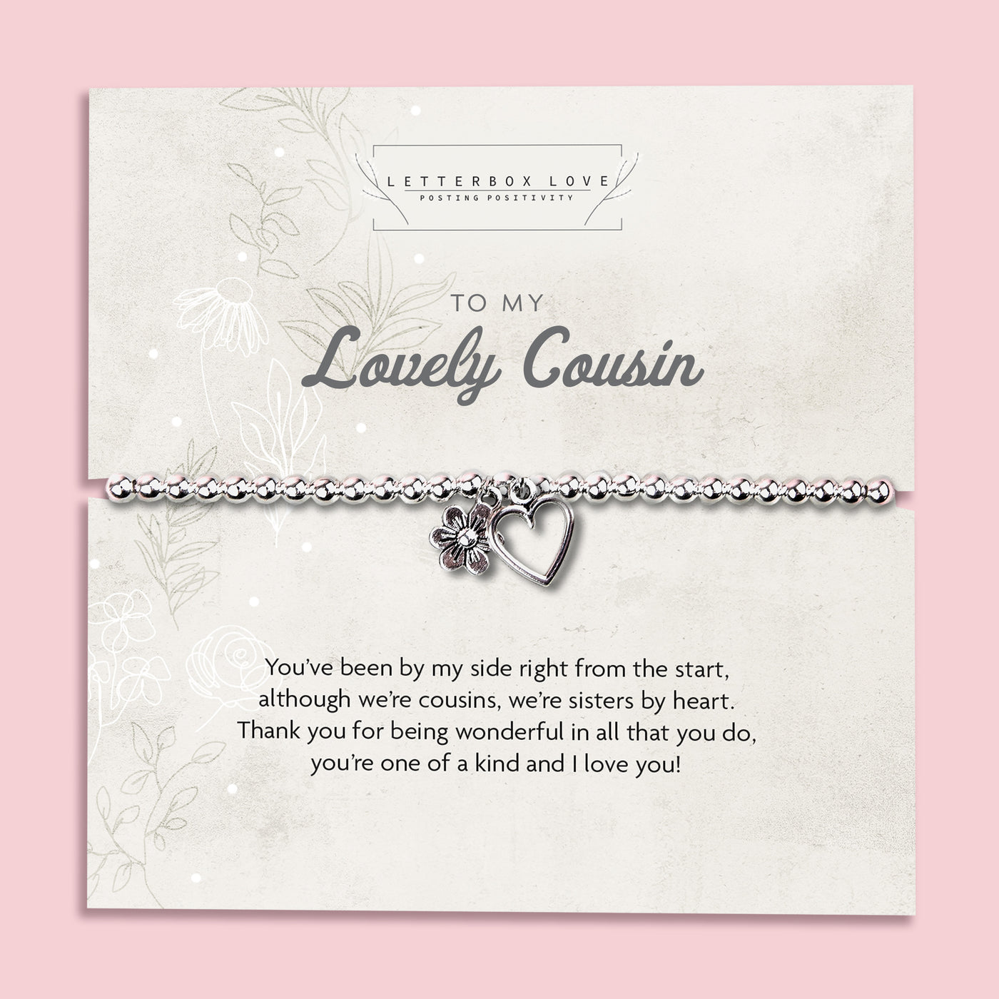 A silver beaded bracelet with a heart and flower charm displayed on a card reading 