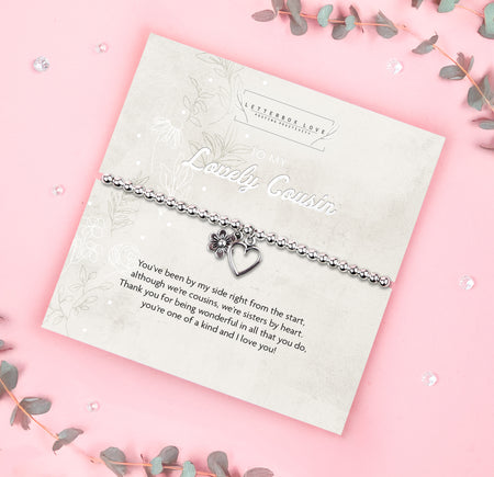 A silver beaded bracelet with a heart and flower charm displayed on a card reading 