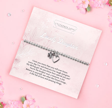 A silver beaded bracelet with a heart and flower charm displayed on a card reading 