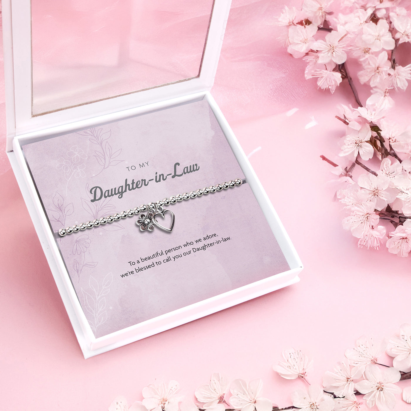 
A silver-plated beaded bracelet with a heart and flower charm displayed in a premium white keepsake box. The backing card inside is soft pink with the title 