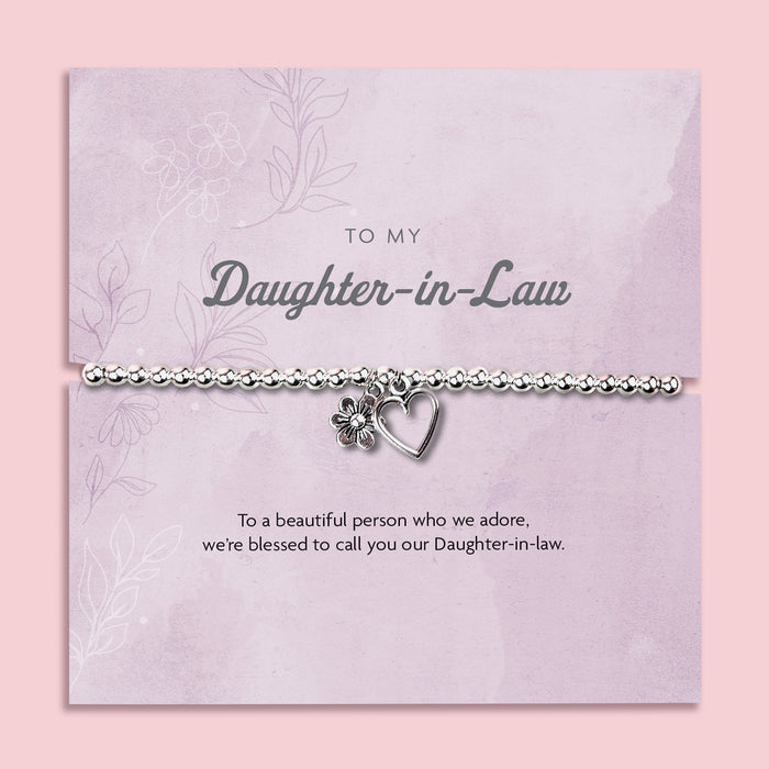 A silver-plated beaded bracelet with a heart and flower charm displayed in a premium white keepsake box. The backing card inside is soft pink with the title "To My Daughter-in-Law" and a heartfelt message beneath it. Surrounded by delicate pink blossoms, creating a warm and thoughtful presentation.