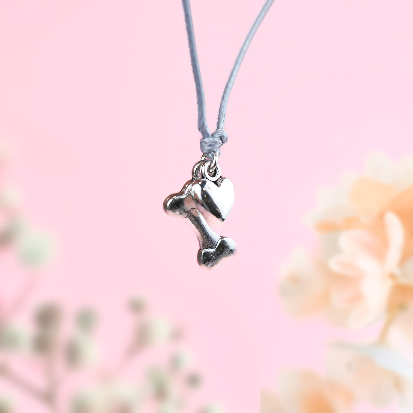 Silver-plated bone and heart charms on a grey string chord bracelet, making a cute bracelet gift for dog lovers.