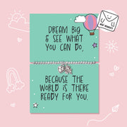 A mint green card bracelet set with motivational quotes, displayed on a pink background with hand-drawn doodles. The top card reads 'DREAM BIG & SEE WHAT YOU CAN DO,' with a silver beaded bracelet and small heart and star charms.