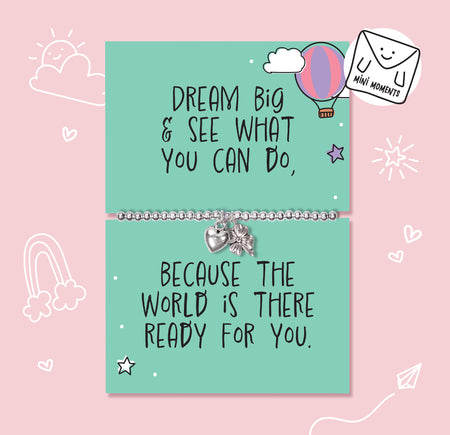 A mint green card bracelet set with motivational quotes, displayed on a pink background with hand-drawn doodles. The top card reads 'DREAM BIG & SEE WHAT YOU CAN DO,' with a silver beaded bracelet and small heart and star charms.