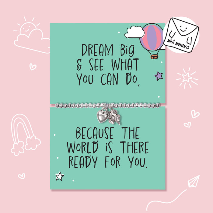 A mint green card bracelet set with motivational quotes, displayed on a pink background with hand-drawn doodles. The top card reads 'DREAM BIG & SEE WHAT YOU CAN DO,' with a silver beaded bracelet and small heart and star charms.