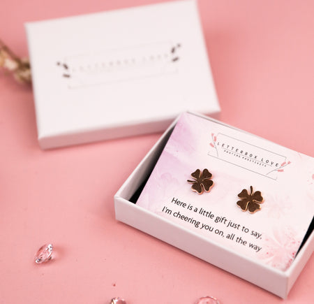 A pair of rose gold four-leaf clover earrings presented in a white box, accompanied by the message 