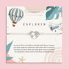 Letterbox Love 'Explorer' travel-themed bracelet – silver heart world map charm on a white cord, displayed on an adventure-inspired card with a hot air balloon, airplane, and uplifting message. Perfect gift for travellers, backpackers, graduates or anyone chasing their dreams. A thoughtful letterbox gift for wanderlust and new journeys.