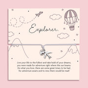 Flat lay of a silver charm bracelet featuring a heart and airplane charm, displayed on a pastel card with hand-drawn travel illustrations and the word "Explorer" a bracelet gift celebrating adventure, gap years and new journeys.