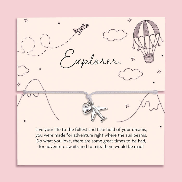 Flat lay of a silver charm bracelet featuring a heart and airplane charm, displayed on a pastel card with hand-drawn travel illustrations and the word "Explorer" a bracelet gift celebrating adventure, gap years and new journeys.