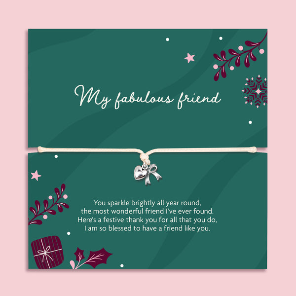 A square green xmas bracelet gift with decorative illustrations and a beige cord across the centre with a silver bow and heart charm. The top half reads 'My fabulous friend' and the bottom half has a festive thank-you message, all on a light pink background.