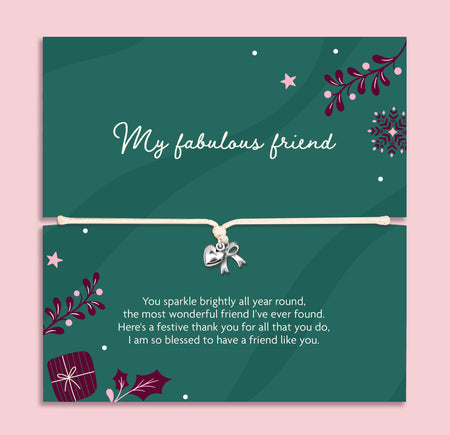 A square green xmas bracelet gift with decorative illustrations and a beige cord across the centre with a silver bow and heart charm. The top half reads 'My fabulous friend' and the bottom half has a festive thank-you message, all on a light pink background.