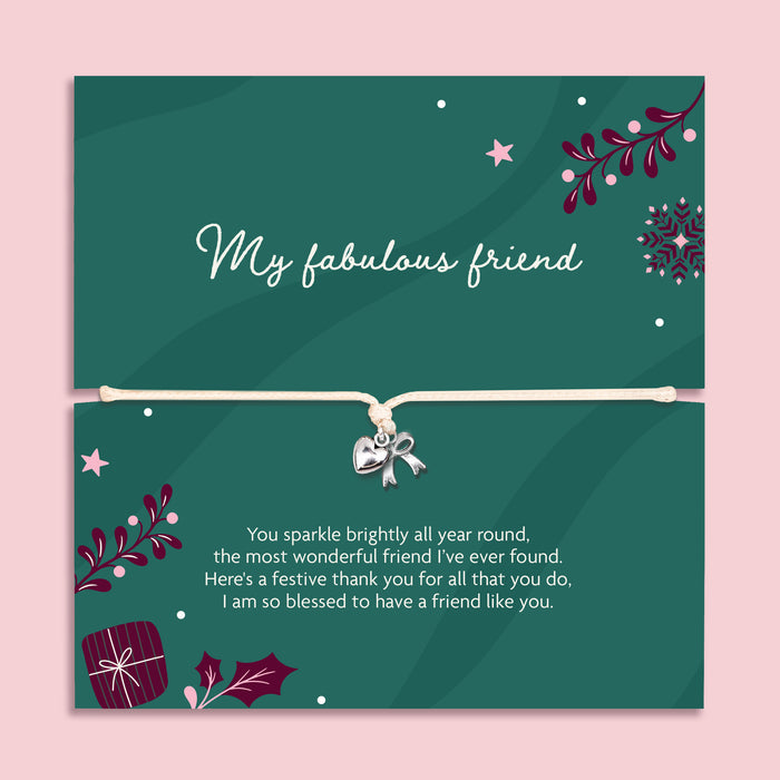 A square green xmas bracelet gift with decorative illustrations and a beige cord across the centre with a silver bow and heart charm. The top half reads 'My fabulous friend' and the bottom half has a festive thank-you message, all on a light pink background.