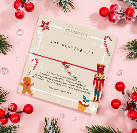 Christmas-themed card titled 'THE FESTIVE ELF' with playful illustrations of a gingerbread man, candy cane, nutcracker, and cupcake. The card features a cheerful message from a mischievous elf and is adorned with a red and white cord tied in a bow.