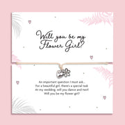 Card with 'Will you be my Flower Girl?' question and heart and flower bracelet on a pink background