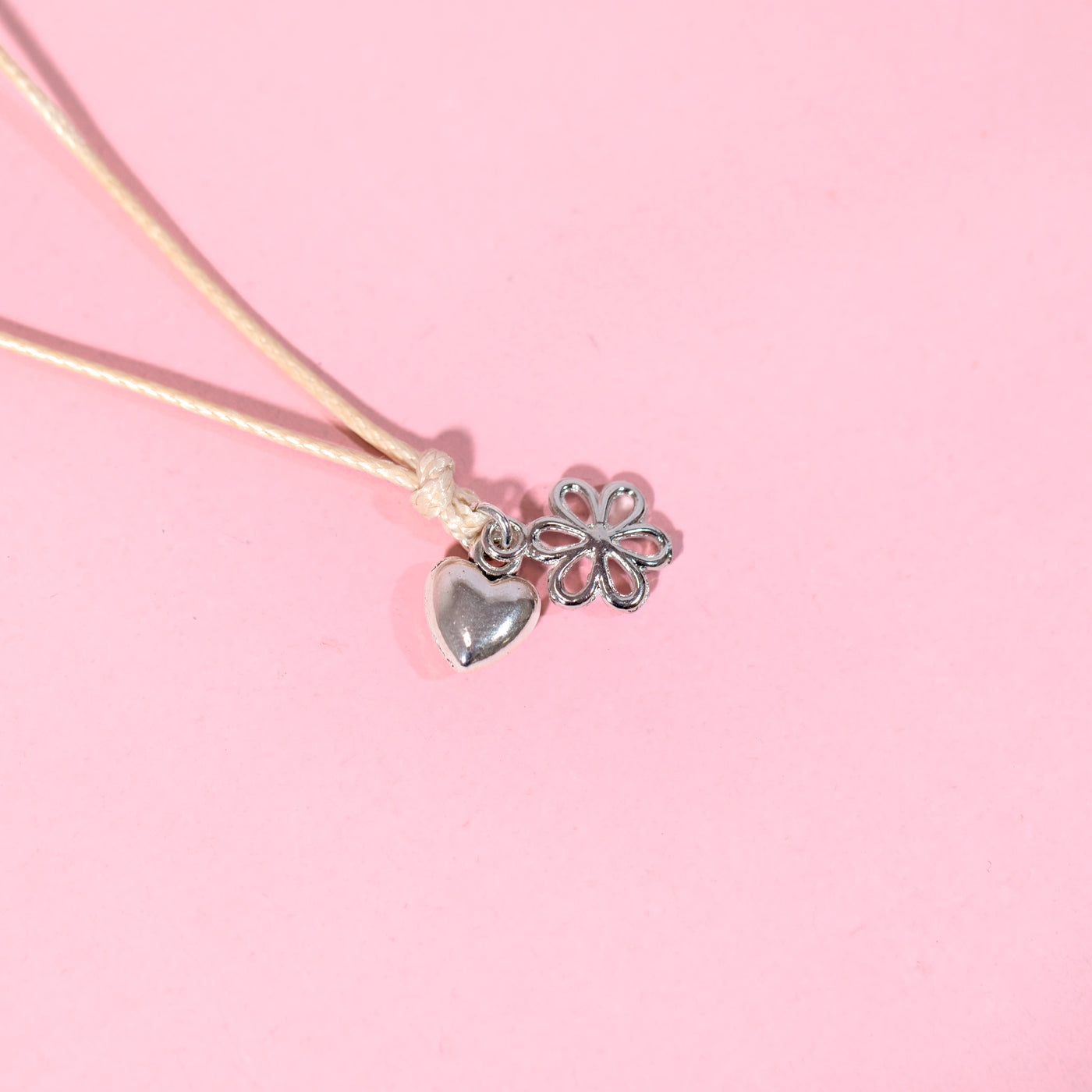 Necklace with heart and flower charms on a pink background