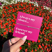 A hand holds a bright pink card with white text reading 'Always my sister.