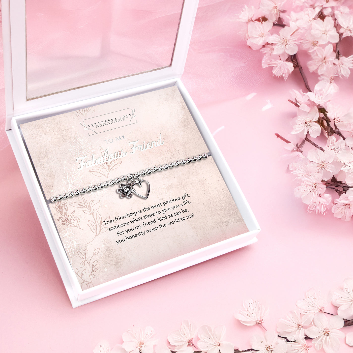 Silver beaded bracelet with heart and flower charms, displayed in a white gift box alongside a card titled 