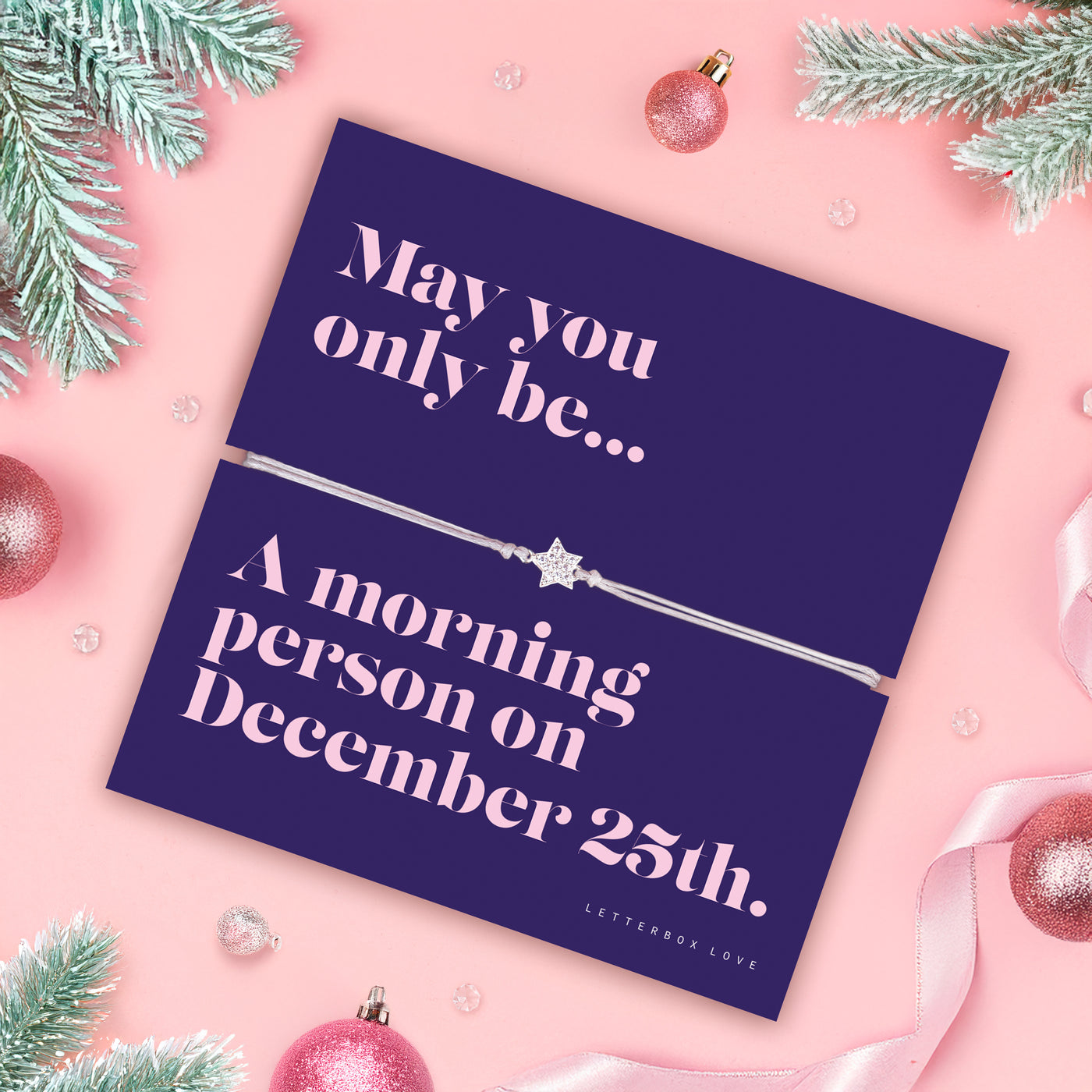 Purple card with a quote and a beautiful bracelet on a pink background with Christmas decorations. An affordable friendship bracelet for Christmas